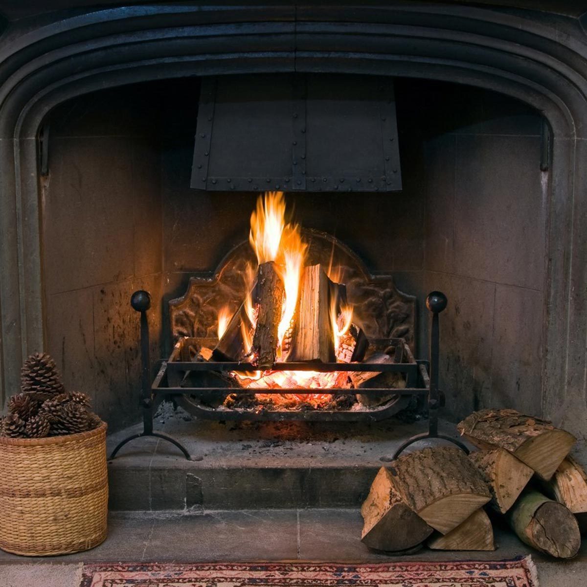 fire within a large stone arched fireplace, with pile of logs and basket of pine kernels fireplace fire