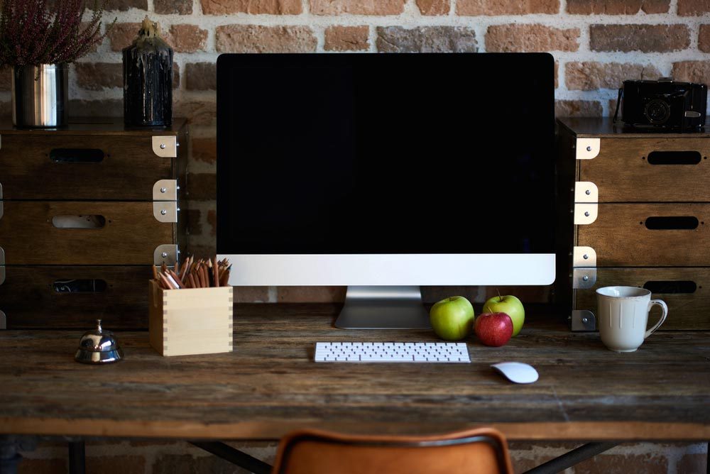 Desktop in modern loft interior with advanced computer for perfect creative freelance work and stationary, mock up PC standing near cup of coffee and croissant for breakfast in co working office