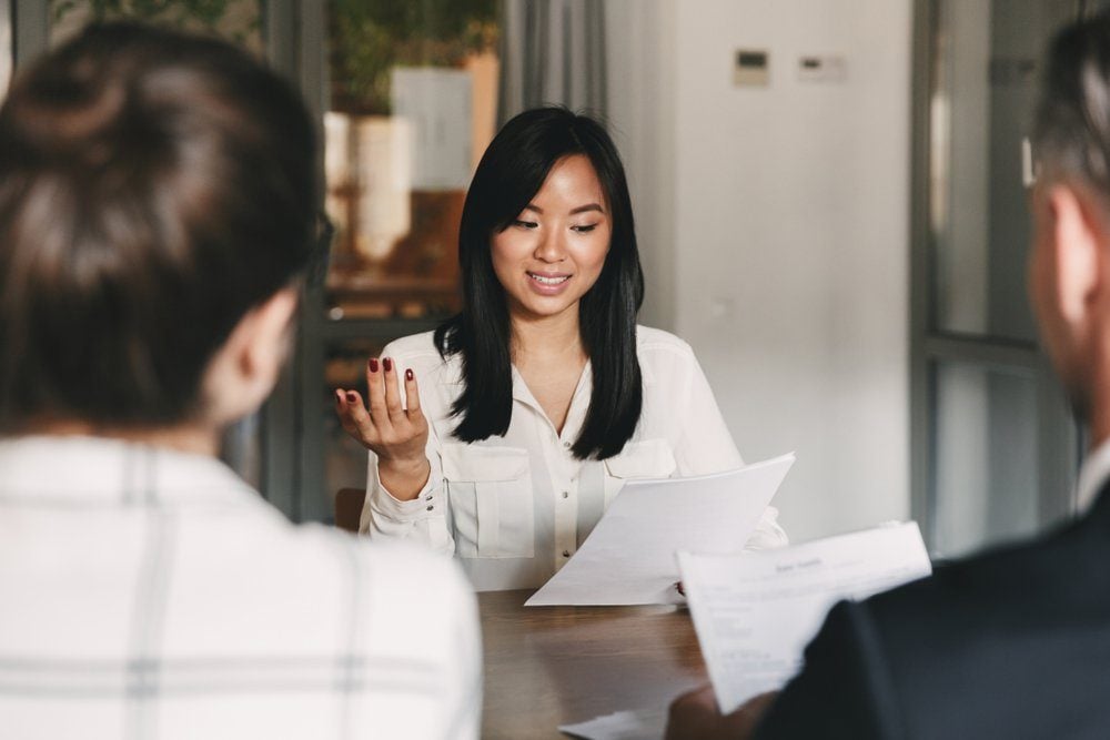 Business, career and placement concept - businesslike asian woman holding resume and speaking to employers of big company during corporate meeting or job interview