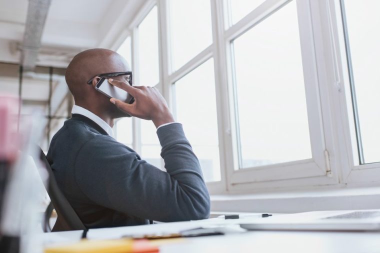 Young african man sitting at his desk talking on his mobile phone in office. African executive using cell phone while at work.