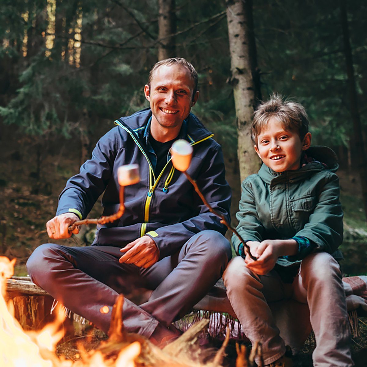 Father & son agree meal planning for group camping makes trips so much better as they roast marshmallows over the campfire