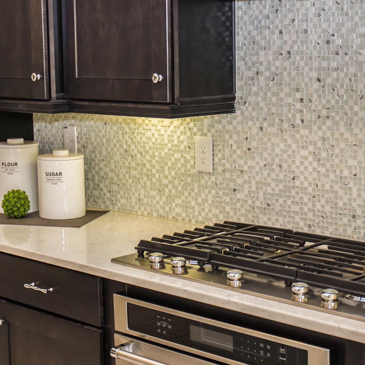 small white and grey square tile mosaic backsplash with a light countertop and black cabinets