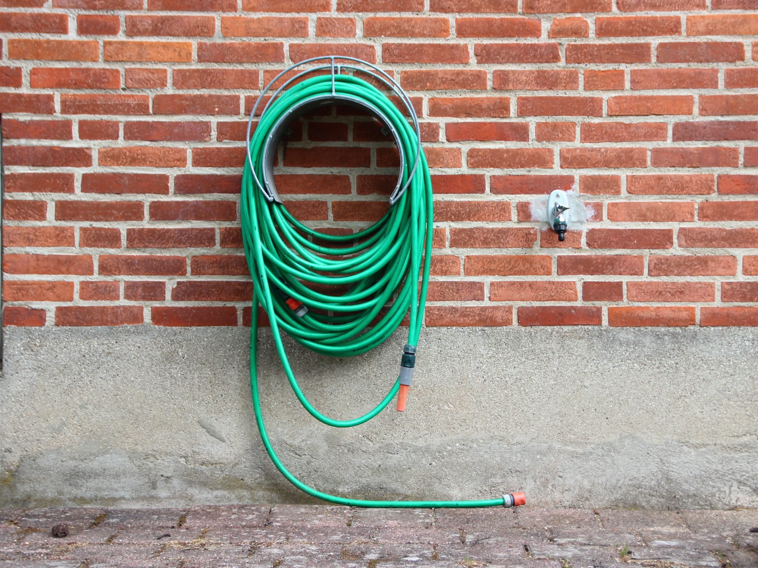 Green Garden Water Hose Hanging on Red Brick wall. Not connected to Water Tap.