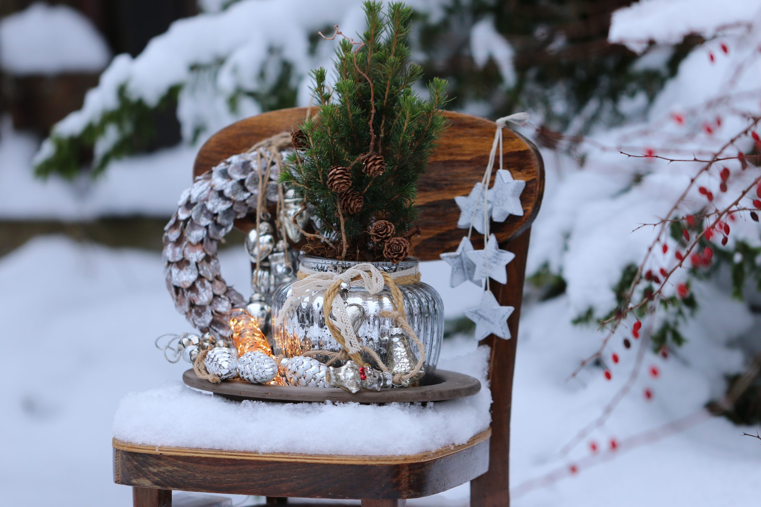 Winter composition with Christmas wreath, glass decoration, garland, fir tree, wooden star on vintage wooden child chair on snow, natural background, outdoor and space, scene in snow garden