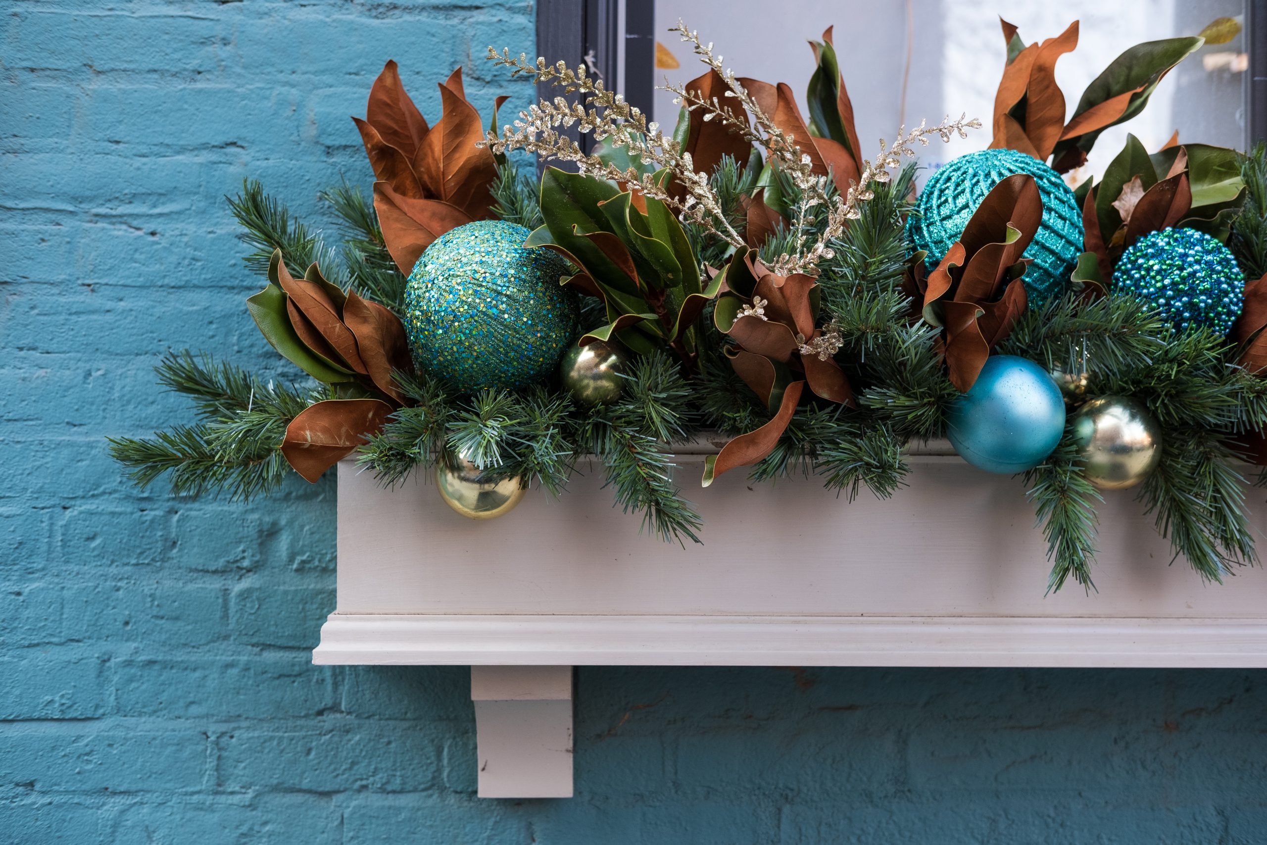 A close-up of the left side of a window planter box decorated for Christmas, set against a bright blue brick building.