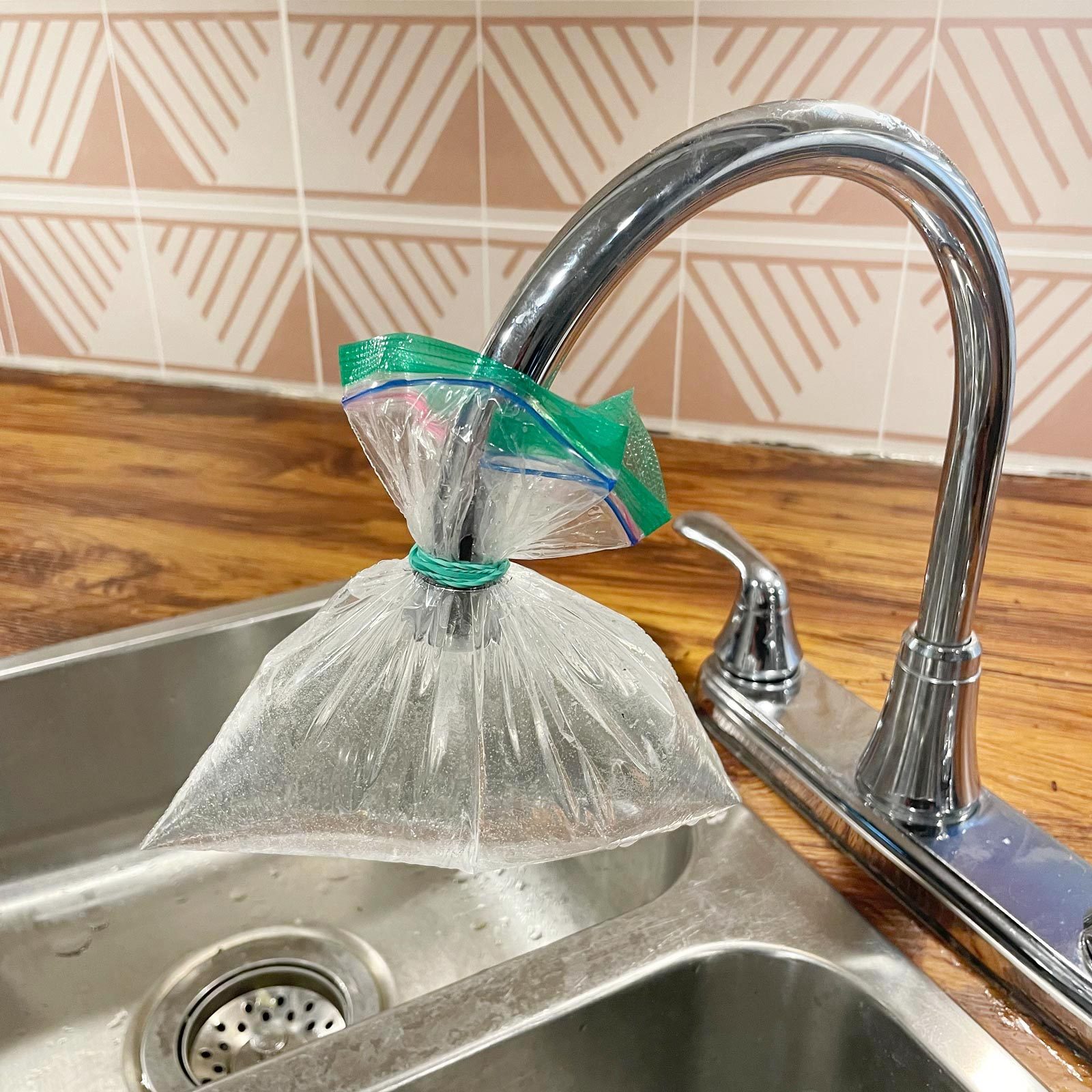 a plastic bag filled with vinegar being held onto a kitchen sink faucet with a rubber band
