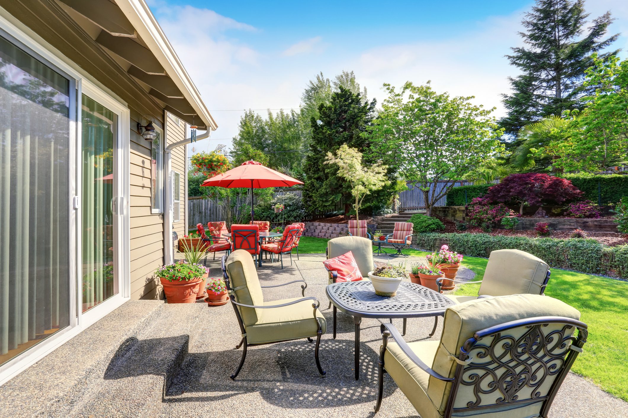 Well kept garden and backyard area with concrete floor patio and various outdoor furniture set up