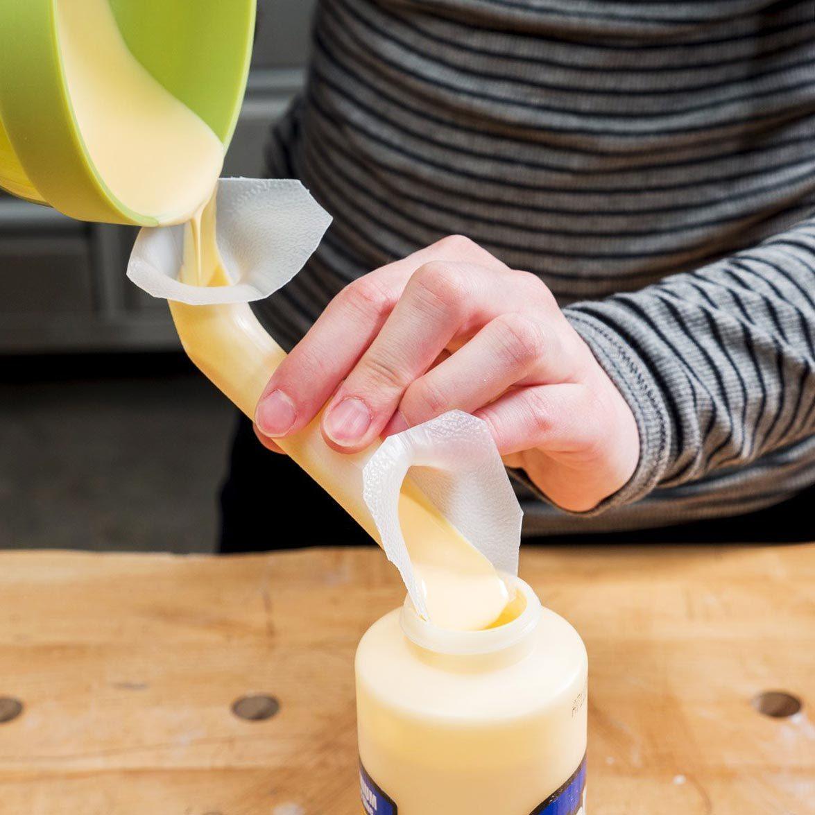 close up of hands using a Milk Jug as a Funnel to pour glue into a small container