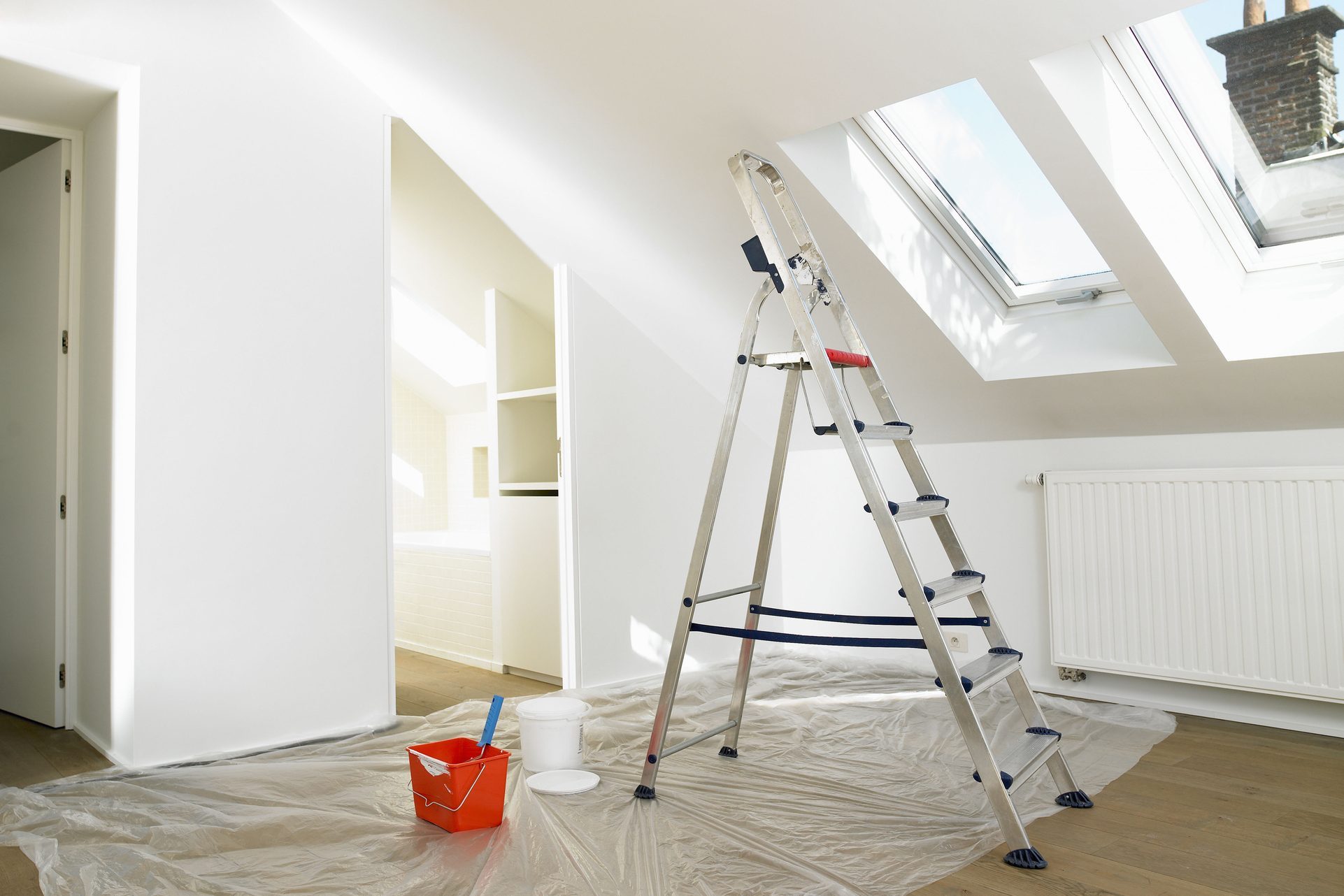 a room with slanted ceilings, a ladder, and a bucket of primer