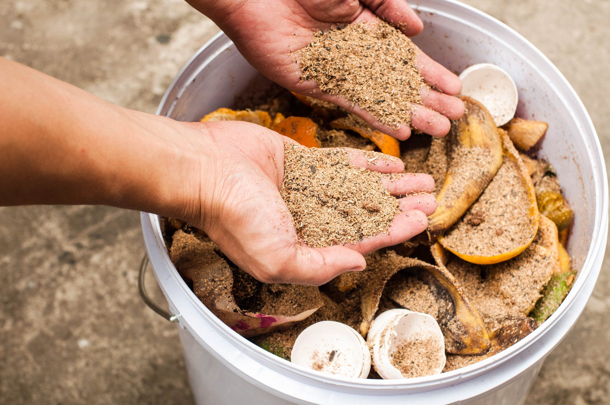 A young person is composting kitchen leftovers on a recycled plastic bin outdoors