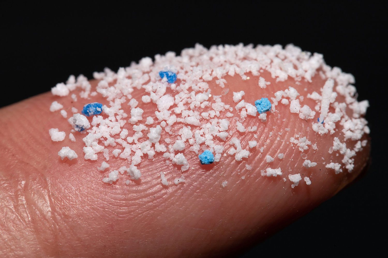 Small miiroplastic Pellets On The Finger on a black background