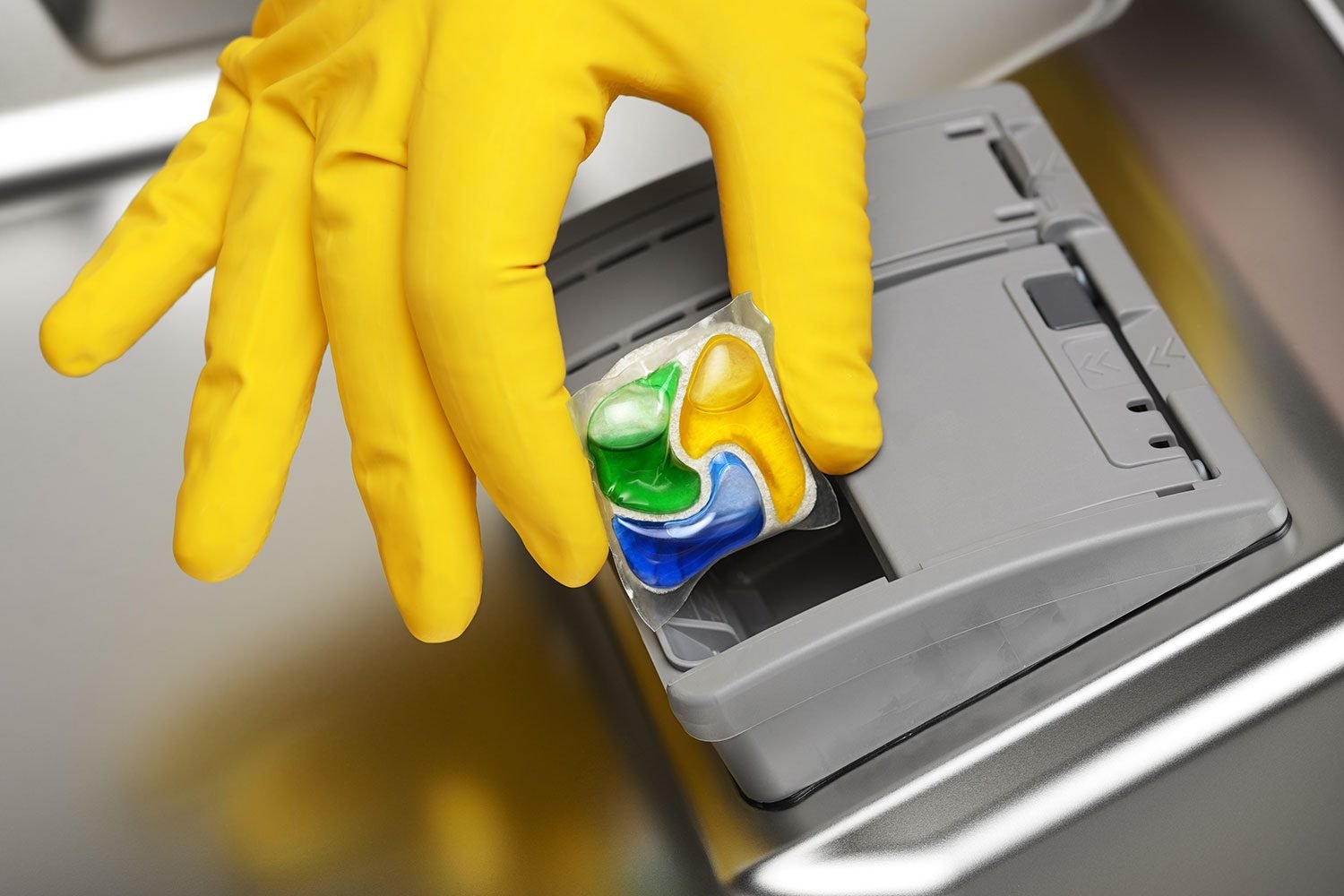 Close-up of hand in yellow rubber glove putting detergent tablet into dishwasher