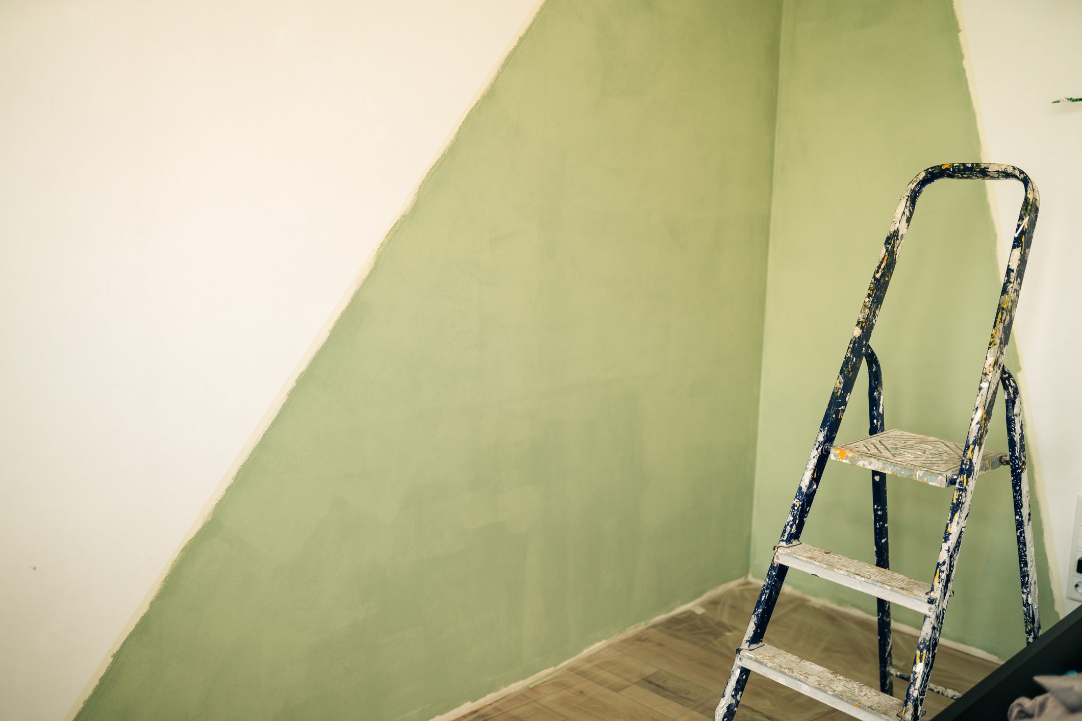 Paintbrush on can on top of step ladder with painted wall.