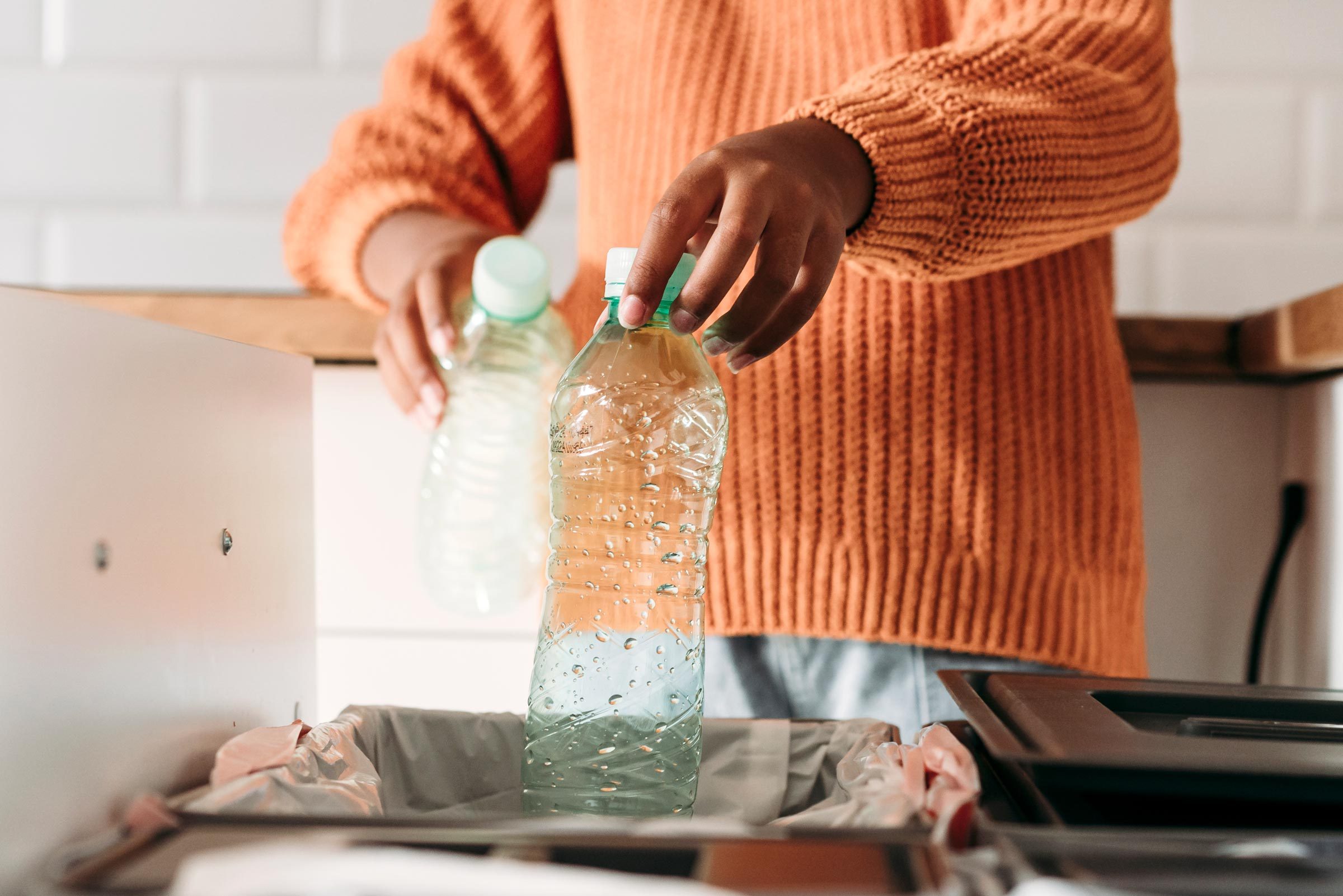 Hands of girl putting plastic bottles in recycling bin at home