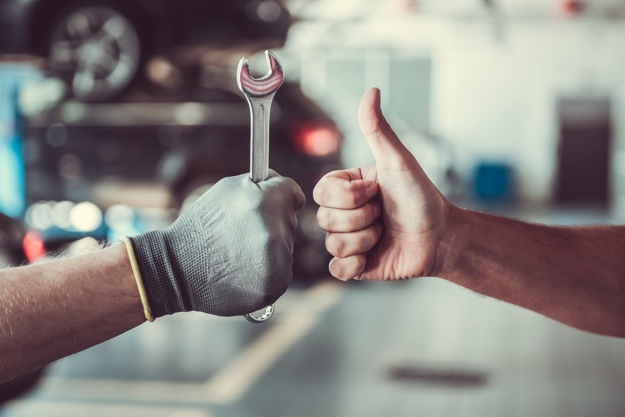 Mechanics Working in an Auto Repair Service Center, With One Hand Holding a Wrench and the Other Giving a Thumbs Up