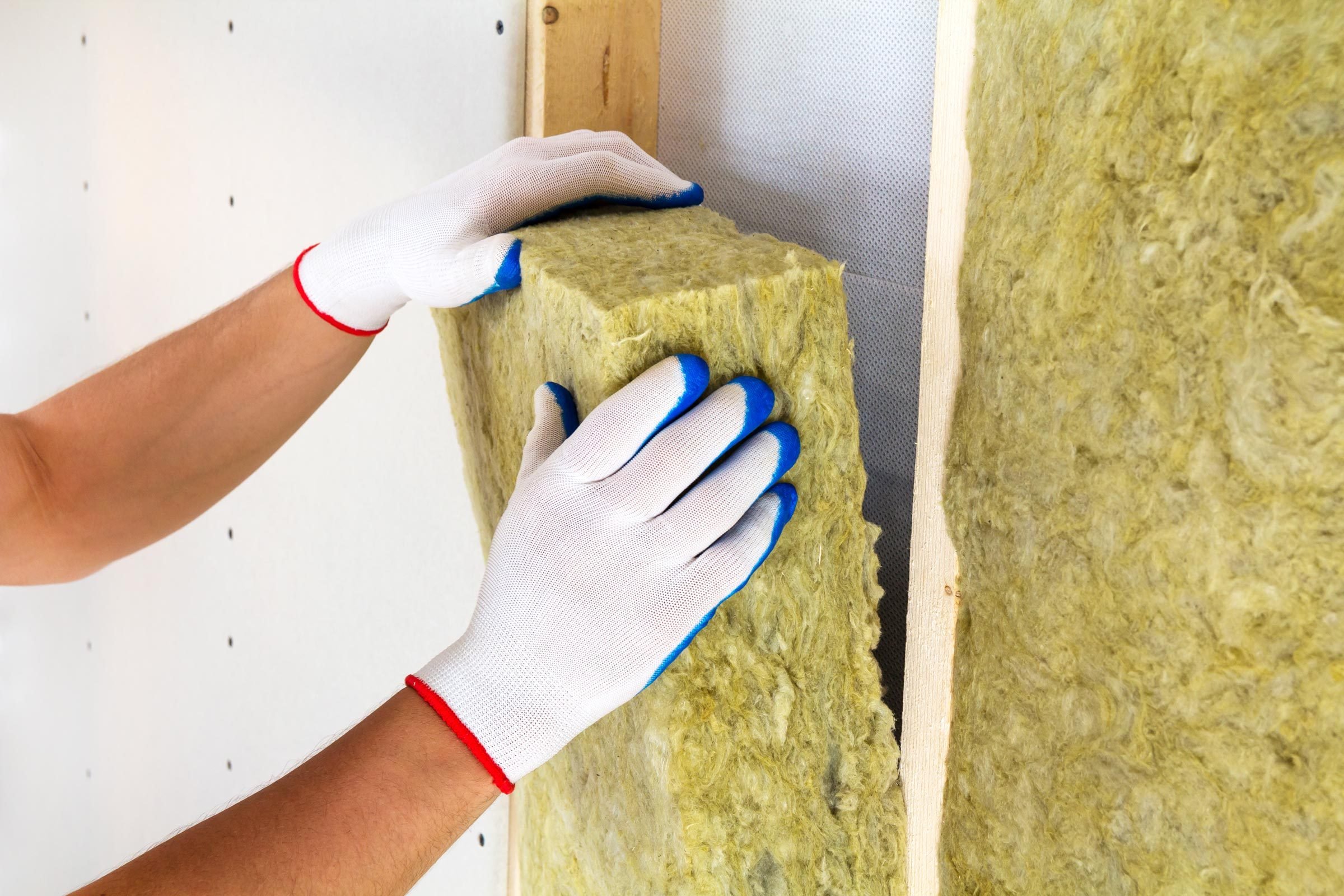 Close-up of worker hands in white gloves insulating rock wool insulation staff in wooden frame for future walls for cold barrier. Comfortable warm home, economy, construction and renovation concept.