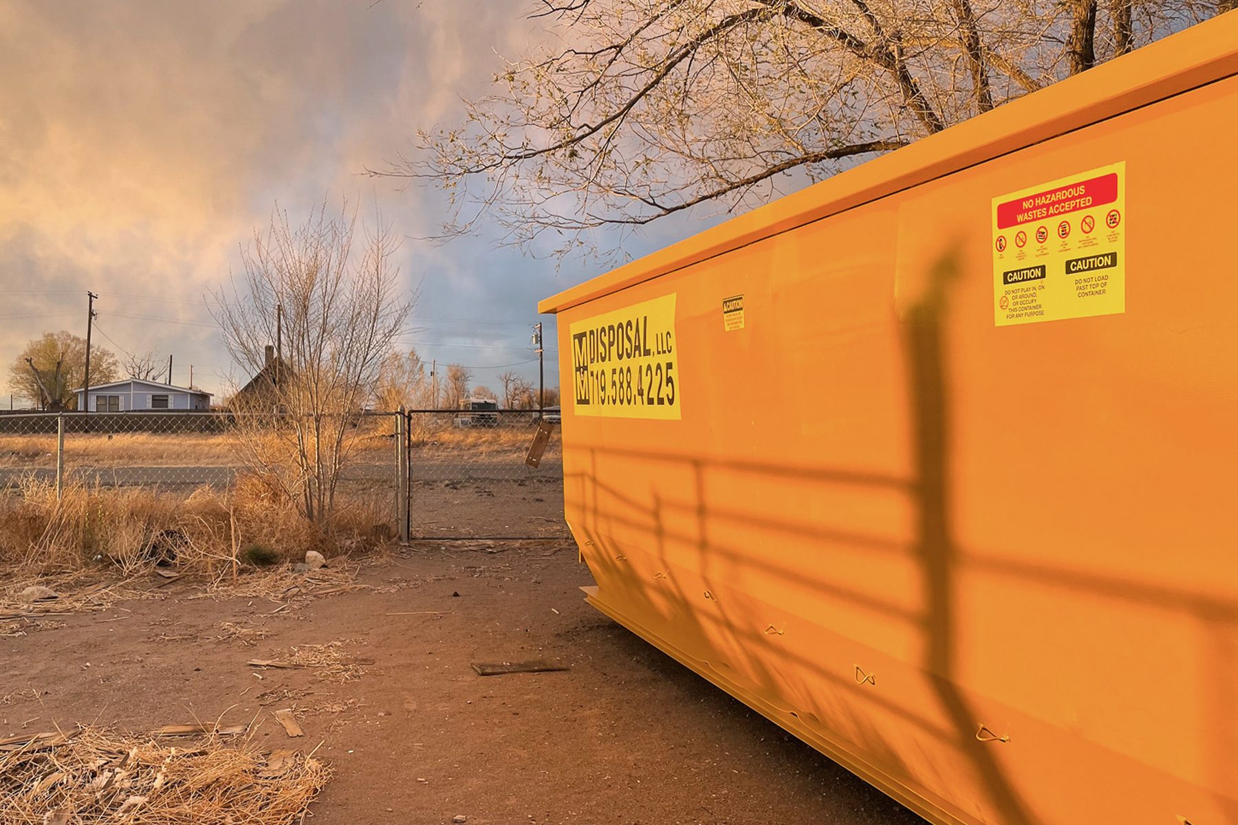 An orange dumpster on the side during a sunset