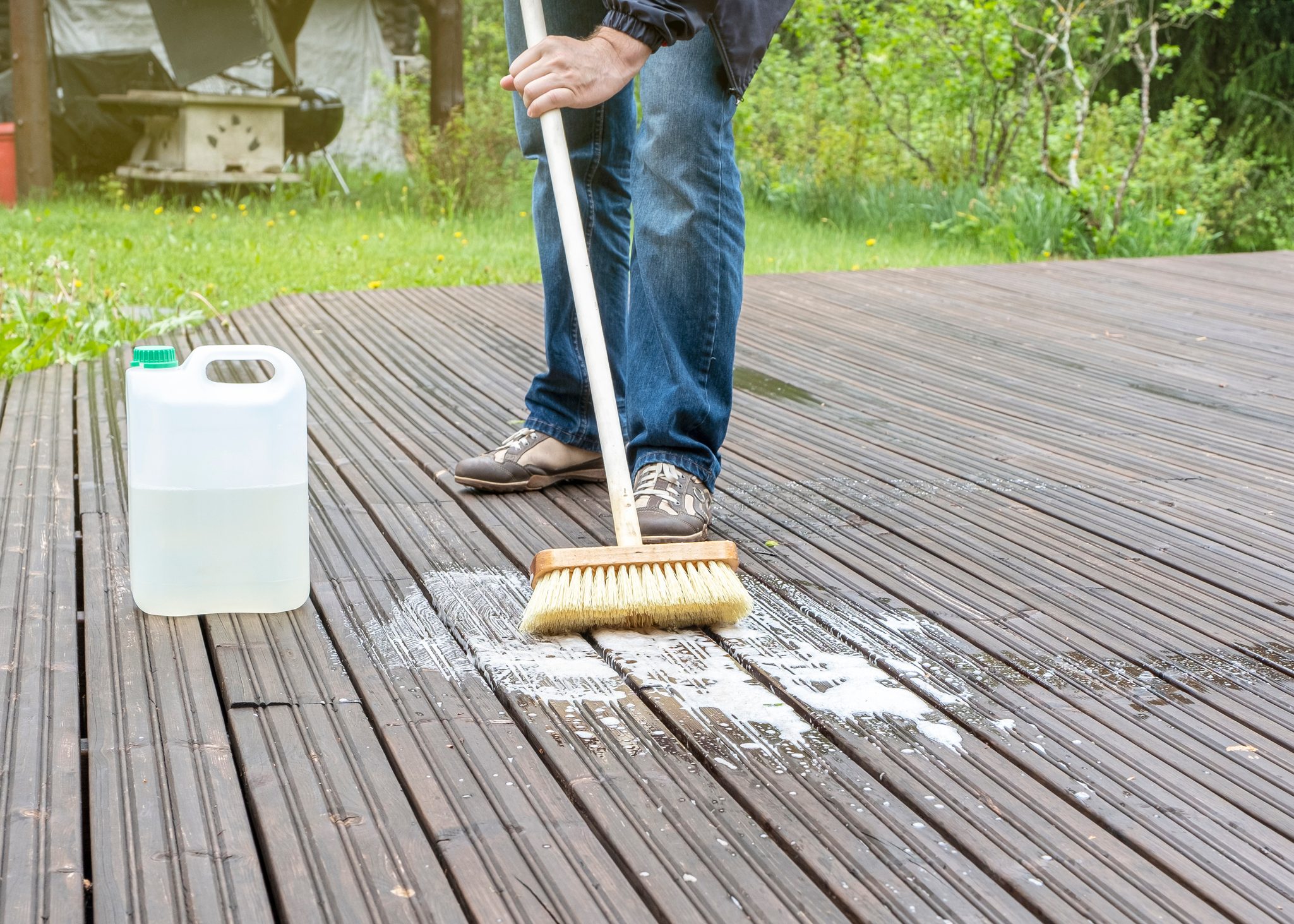 A man is cleaning with soapy water and brushing the wooden floor of the terrace.