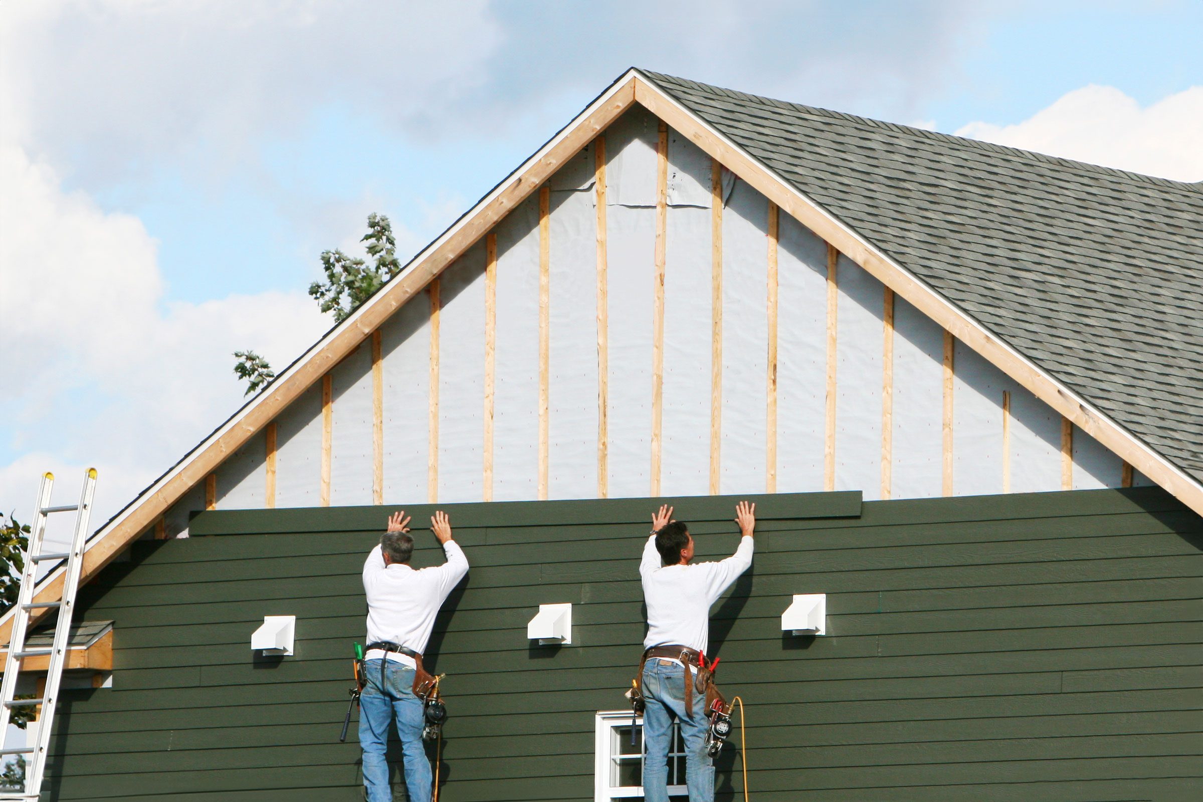 two workers adding new siding to the exterior of a green home