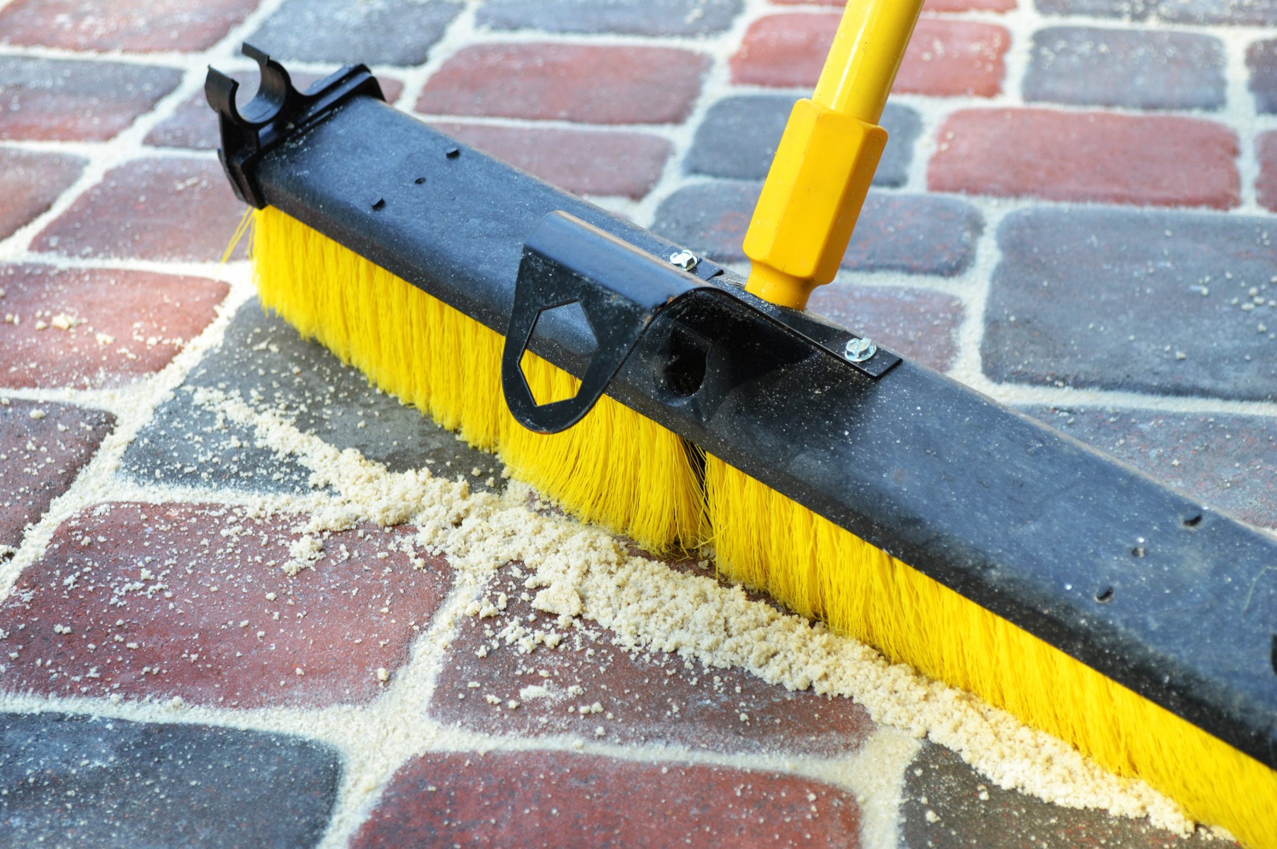 Broom Sweeping Sand into Brick Pavers