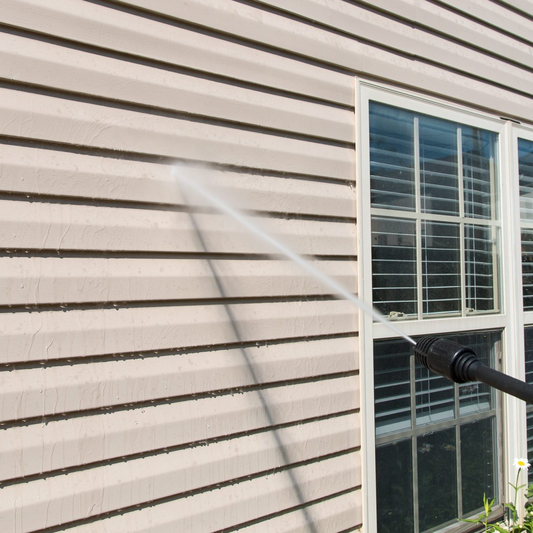 Power washing. House wall vinyl siding cleaning with high pressure water jet.