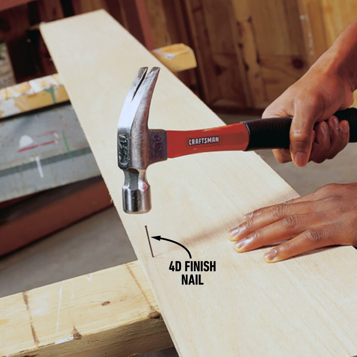 A person using a hammer to drive a 4D finish nail into a piece of wood. The hammer has a black and red handle, and there are wooden structures in the background. An arrow and text label identify the nail as a 4D finish nail.