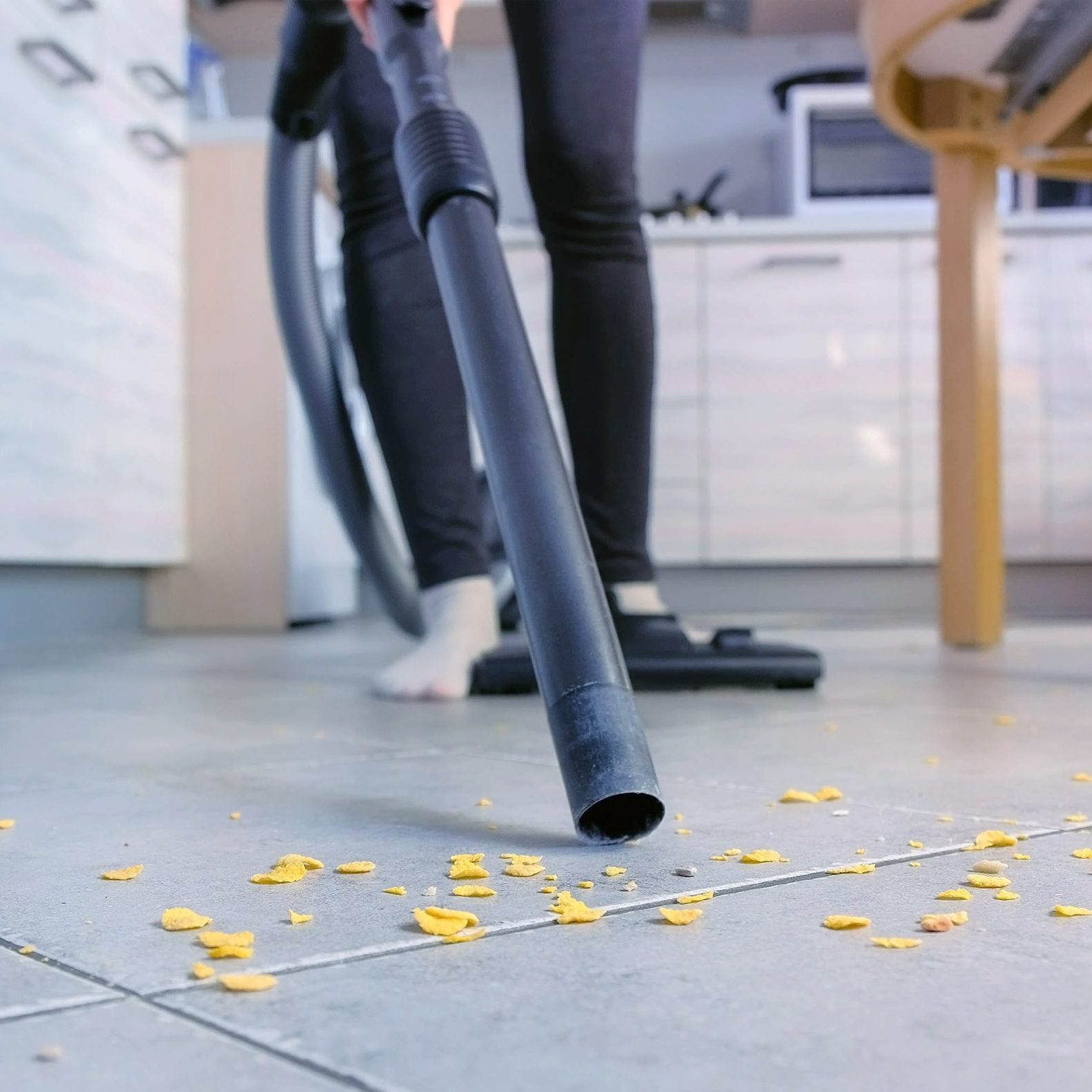 Woman is vacuuming the kitchen floor without brush, only pipe. Legs close-up.