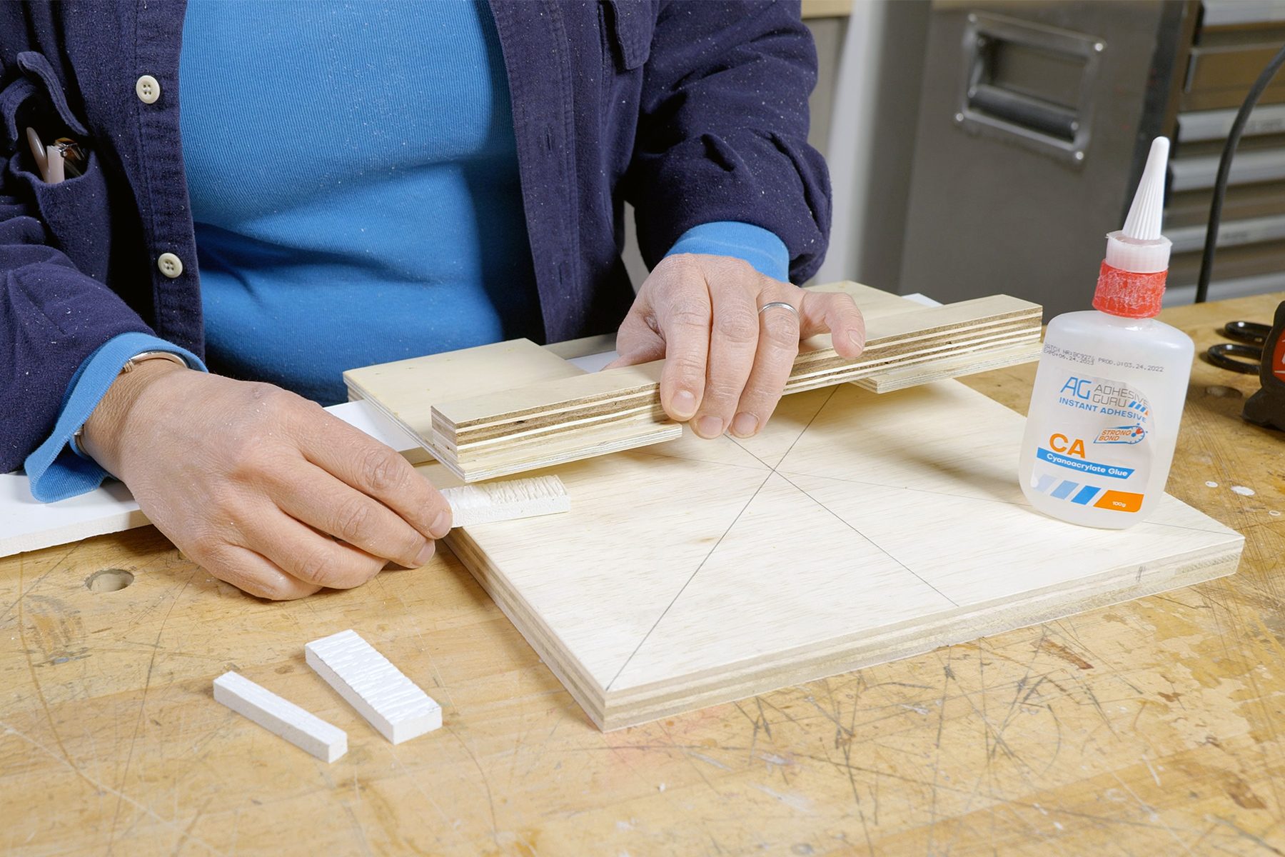 Person working on a woodworking project using glue and wooden pieces, with a clamp securing parts on a workbench.