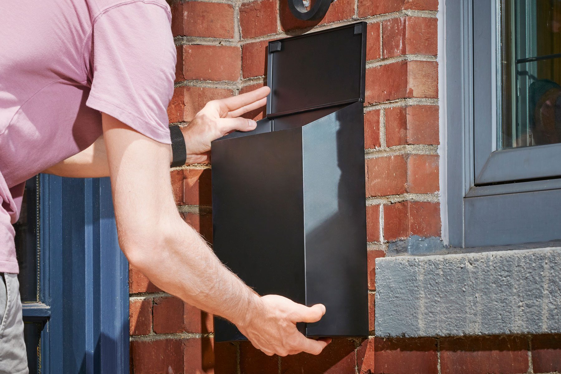 A person can be seen attaching a mailbox to the wall.