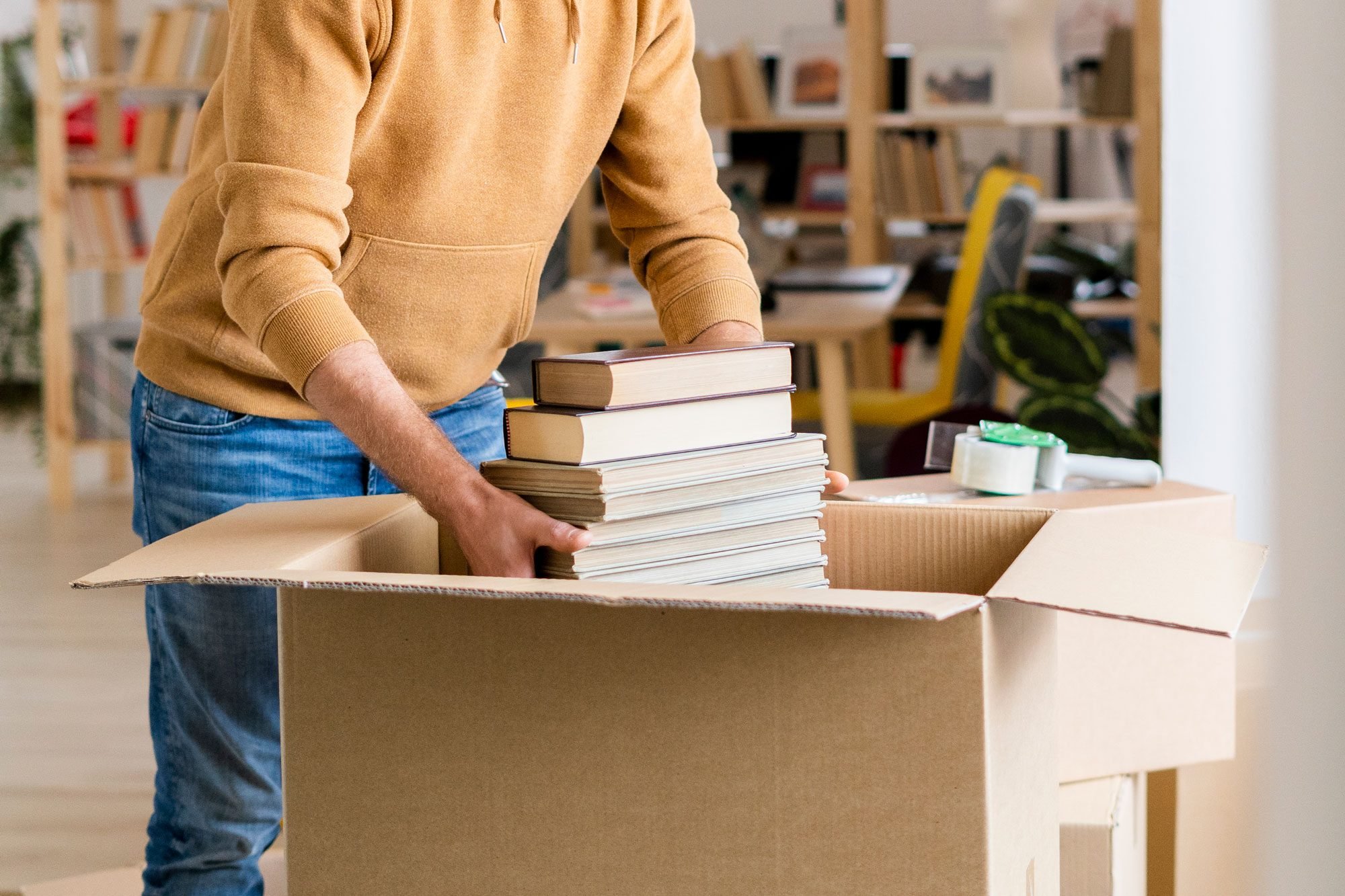 Young Man Packing Books In Cardboard Box