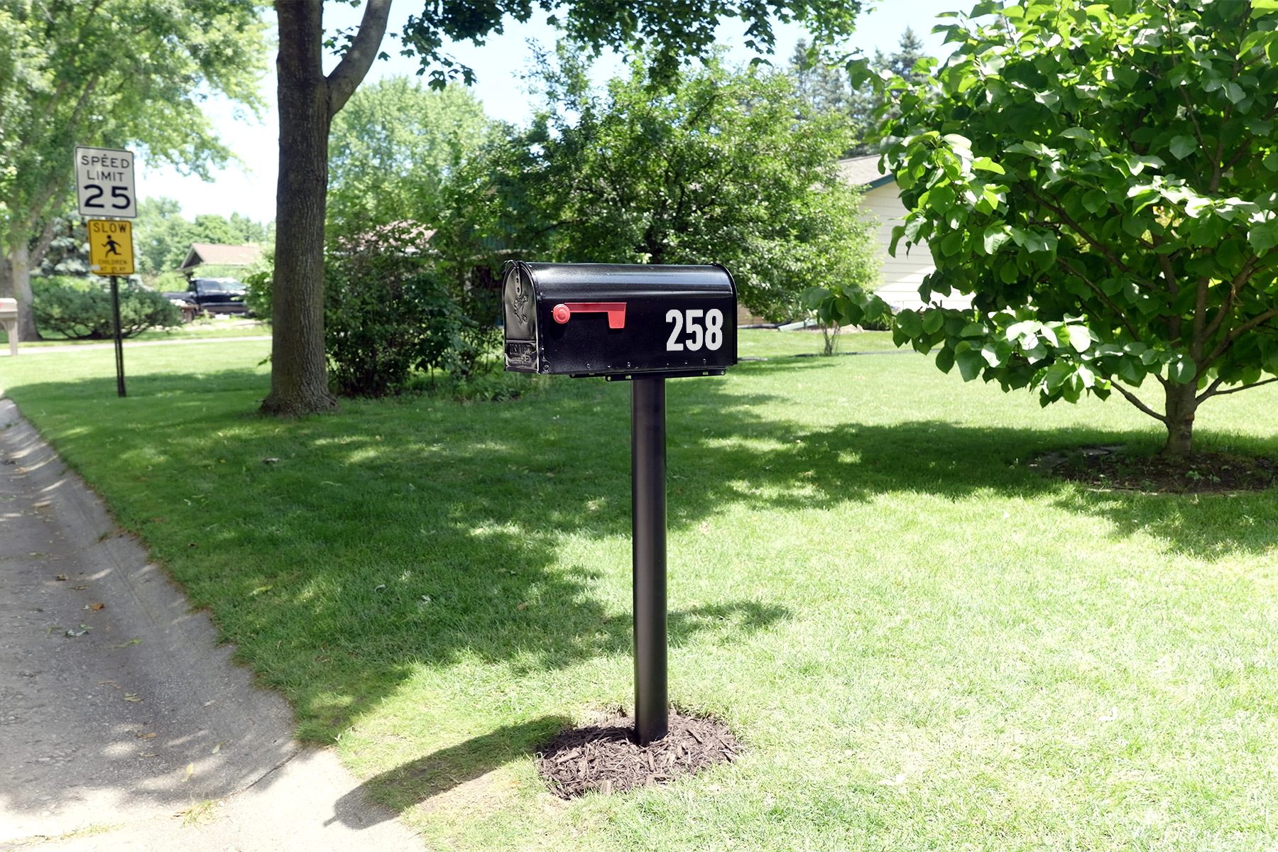 A black mailbox labeled with the number 258 stands on a neatly maintained lawn near a tree. In the background, a sign indicating a speed limit of 25 mph is visible along the road.